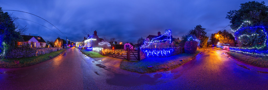 The Besselsleigh village lights in panoramic view in cloudy twilight. A damp road reflects the Christmas lights making the scene even more atmospheric and suggestive of warmth and comfort in winter. Copyright Nikhilesh Haval, 2015.